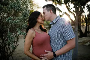 Eyes Closed Prints: Husband kissing pregnant wife on nose while standing in park during sunset