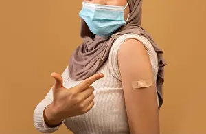 Unrecognizable Prints: I got my covid-19 vaccine. Vaccinated muslim lady showing arm after vaccination and pointing at plaster