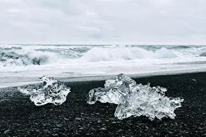 Iceberg pieces on black Diamond beach near Jokulsarlon lagoon, Iceland. Atlantic ocean waves and cloudy sky on background. Landscape photography