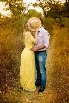 Kiss Prints: image of a guy and a girl kissing in the park hiding behind a straw hat