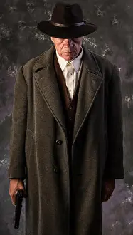 Cliche Prints: Image of sinister looking man wearing overcoat and hat holding automatic pistol to one side against portrait background