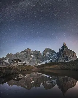 Incredible night landscape with a reflection of starry sky and mountains in a water of small lake in a popular tourist destination - Baita Segantini