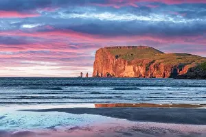 Incredible sunset in low tide time on Atlantic ocean coast near village Tjornuvik. Famous rock formations Risin and Kellingin Eidiskollur on backgroun