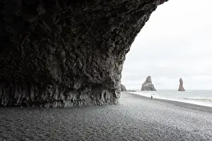 Incredible view on Black beach and Troll toes cliffs in cloudy weather. Lonely tourist with tripod going on coastline. Reynisdrangar, Vik, Iceland