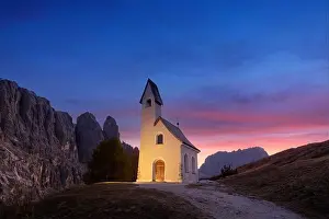 Incredible view on small iIlluminated chapel - Kapelle Ciapela on Gardena Pass, Italian Dolomites mountains. Colorful sunset in Dolomite Alps, Italy