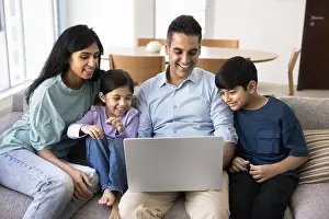 Siblings Prints: Indian couple and kids watching on-line movie using laptop