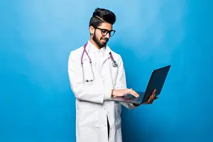 Practitioner Prints: Indian doctor standing in the studio while working with laptop