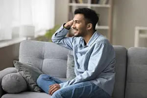 Satisfied Prints: Indian guy relaxing seated on sofa smiling looking out window