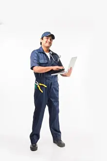 Indian happy auto mechanic in blue suit and cap holding spanner tool in action, isolated over white background