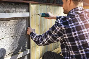 Screwdriver Prints: installing wooden planks on concrete block wall at home backyard
