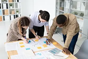 Professional Occupation Prints: Three intercultural colleagues with highlighters bending over table with papers