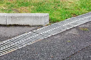 Grille Prints: iron grid drainage system on an asphalt road with a curb on the side of the road green grass