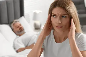 Awake Prints: Irritated woman covering her ears in bed at home. Problem with snoring husband