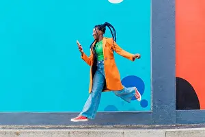 Braids Prints: Italy, Milan, Woman with braids jumping against blue wall