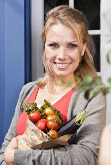 Differential Prints: Italy, Tuscany, Magliano, Young woman holding bag of vegetables, smiling, portrait