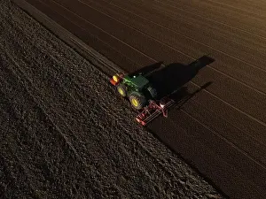 A John Deere Tractor seeds a previously cultivated field with sweetcorn, late in the evening