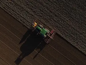 A John Deere Tractor seeds a previously cultivated field with sweetcorn, late in the evening