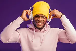 Black Man Prints: Joyful happy hipster man in white hoodie and yellow hat listening music with headphones