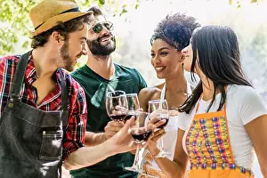 Toasting Prints: Joyful multiracial friends at picnic celebrating toasting with red wine standing under the trees in the nature - wine