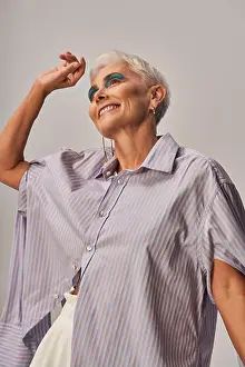 Vogue Prints: joyful and trendy senior woman with bold makeup and short silver hair looking away on grey backdrop