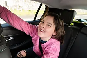 Seatbelt Prints: A joyful young girl in a pink shirt, smiling and waving with excitement during a car ride