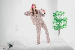 Awake Prints: Joyful young woman in polka dot pajamas dancing on a cozy bed while listening to music in a bright bedroom