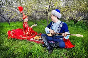 Almaty Prints: Kazakh woman with tea and man playing dombra instrument on the green grass in apple garden of Almaty