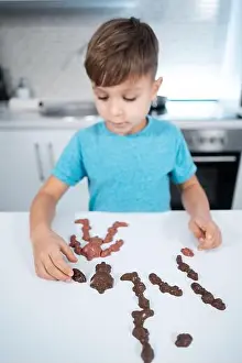 Taking Prints: kid boy play with chocolate sweets or candies on table at modern home kitchen
