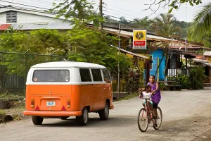 Street Life Prints: Two kids riding a bike on the street with an orange VW bus Puerto Viejo, Costa Rica