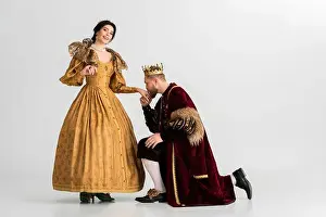 Knee Prints: king with crown bending on knee and kissing hand of smiling queen on grey background
