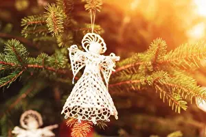 Knitted Prints: Knitted toy angel on a fir tree in sunlight. Christmas concept. Closeup