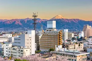 Kofu, Japan city skyline with Mt. Fuji peaking over the mountains at dusk