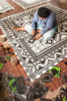 High Angle View Prints: Koto Tawake printing stencils onto bark cloth made by beating the inner white bark of the paper mulberry bush