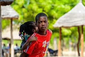 KOUTAMMAKOU, TOGO - JAN 13, 2017: Unidentified Togolese boy in red shirt carries his little sister in the village