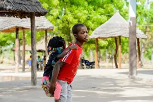 Nigerian Prints: KOUTAMMAKOU, TOGO - JAN 13, 2017: Unidentified Togolese boy in red shirt carries his little sister in the village