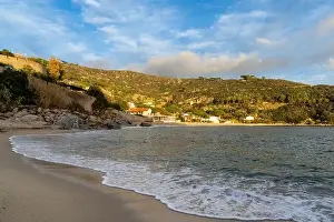 A landscape view of Cavoli Beach on Elba in warm evening light and boulders in the foreground