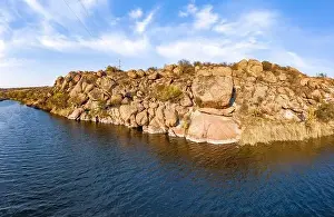 Among the large boulders, a smooth shining stream flows in the evening warm light in picturesque Ukraine