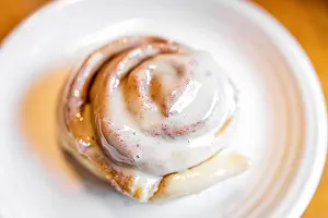Vanilla Prints: One large cooked baked cinnamon bun roll swirl dessert on white plate with sugar crust on kitchen table