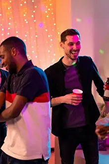 Descent Prints: Laughing guy with red glass dancing and enjoying home party with friends with African man in t-shirt having fun near by