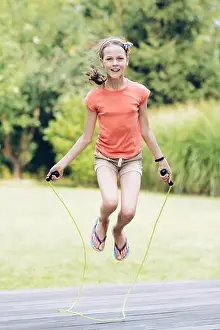 Laughing teenage girl jumping rope in the garden on the terrace in summer