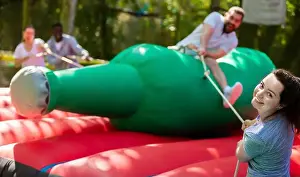 Pulling Prints: Laughing young woman pulling rope of inflatable rodeo bottle, trying to throw friend off