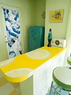Fifties Prints: Lava lamp on lemon patterned worktop in fifties style kitchen with blue patterned roller blind on glass door