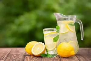 lemonade in glass and jug on wooden table outdoors. Summer refreshing drink. Cold detox water with lemon