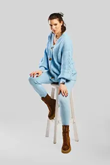 Stool Prints: Full length portrait of beautiful woman in light blue warm knitted tracksuit sitting on stool over grey background