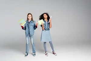 Pupils Prints: full length view of fashionable multicultural schoolgirls standing with books on grey