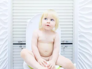 Flirt Prints: A little blonde girl with a mischievous look sits on the toilet in a brightly lit toilet room