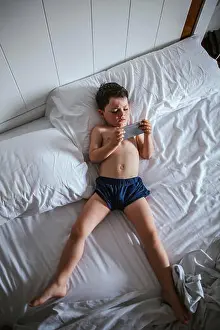 Bedding Prints: Little boy lying on bed using smartphone