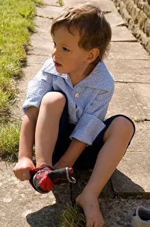Concentrating Prints: Little boy sitting on a stone path putting on a sock