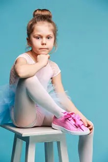 Sneakers Prints: The little girl as balerina dancer sitting on white wooden chair at blue studio background at sneakers