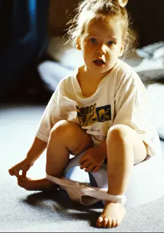 Little girl on potty with underwear around ankles, looking into camera